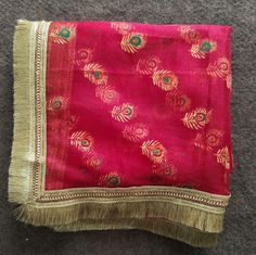 a red and gold scarf with fringes on the bottom, sitting on a gray carpet