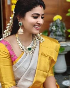 a woman wearing a yellow and white sari with pearls on her neck, sitting in front of flowers