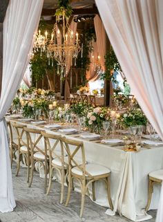 a long table is set up with white linens and greenery for an elegant dinner