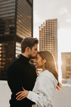 a man and woman standing next to each other in front of tall buildings with the sun shining on them