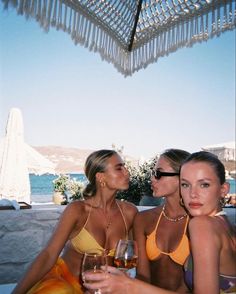 two beautiful women sitting next to each other holding wine glasses in front of the ocean