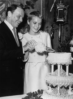 an old black and white photo of a man cutting a cake with a woman standing next to him