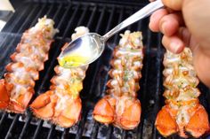 someone is cooking lobsters on the grill with a spoon