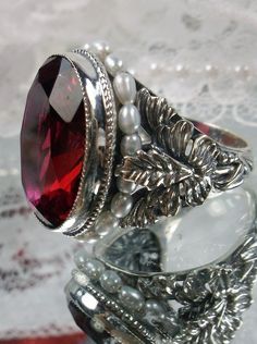 Ruby Red Art Nouveau style sterling silver ring, oval ruby red gem with seed pearls encircling the gem edge and palm tree silver filigree accents on each side of the band Classic Silver Ruby Ring, Silver Ruby Rings For Collectors, Heirloom Silver Garnet Jewelry, Ornate Garnet Ruby Ring As Gift, Classic Ruby Ring With Stone Setting, Vintage Sterling Silver Ruby Ring For Formal Occasion, Oval Engraved Ruby Ring, Oval Ruby Ring Engraved, Collectible Classic Ruby Jewelry