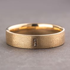 a yellow gold wedding band with a diamond in the center on a gray surface,