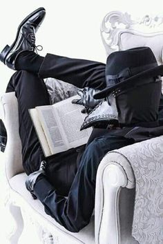 a man in a black suit and top hat sitting on a white chair reading a book