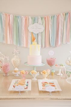 a table topped with lots of desserts next to a cake and bunting banner