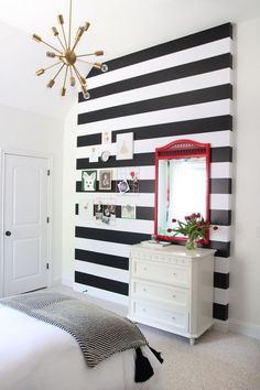 a bedroom with black and white stripes on the wall, a red mirror and dresser