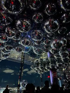 people are standing under large bubbles floating in the air at night, with city lights behind them