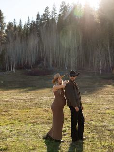 a man and woman standing in the grass with trees in the backgrouds