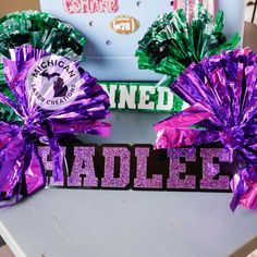 two purple and green cheer bows sitting on top of a table next to each other