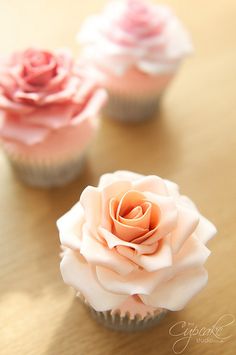 three cupcakes with pink and white frosting on them sitting on a table