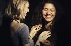 two women standing next to each other smiling and touching their hands on their chests