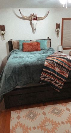 a bed room with a neatly made bed and a cow skull on the wall above it