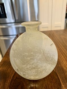 a white glass vase sitting on top of a wooden table next to a refrigerator freezer