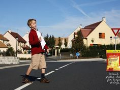 a young boy crossing the street in front of some houses with a bag of chips