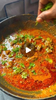 someone is cooking food in a pan with sauce and herbs on the side, while another person holds their hand out to touch it