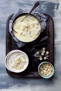 a wooden tray topped with two bowls filled with soup and cashews next to each other