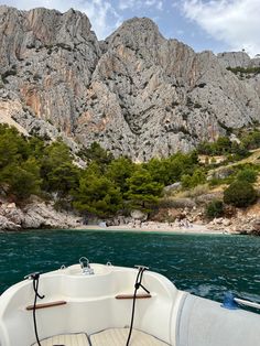 the bow of a boat in front of some mountains and people on the beach below