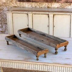 two wooden trays sitting on top of a white table next to a cabinet with drawers