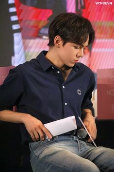 a young man sitting on top of a black chair holding a white object in his hand