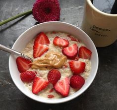 a bowl filled with oatmeal and strawberries next to a cup of coffee