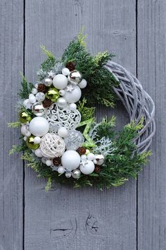 a wreath with ornaments hanging from it on a wooden wall, decorated with greenery and pine cones