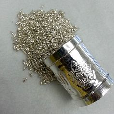 a metal container filled with seeds on top of a white tablecloth next to a pile of silver flakes