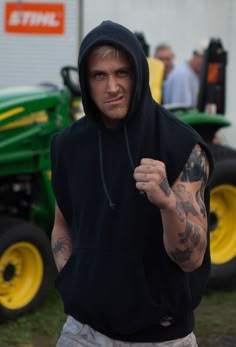 a man in a black hoodie standing next to a tractor and holding his fist up