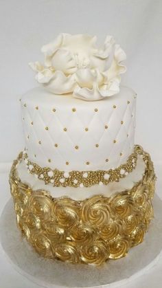 a white and gold wedding cake with flowers on top