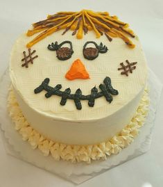 a frosted cake decorated to look like a snowman with orange nose and eyes