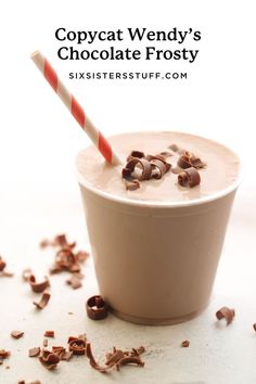 a cup filled with milk and chocolate chips on top of a white table next to a candy cane