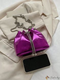 a purple purse sitting on top of a white blanket next to a cell phone and chain