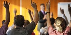 people raising their hands in the air at a conference or seminar, with one person wearing a pink shirt