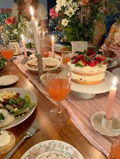 a group of people sitting around a table with plates and food on it, candles in the middle