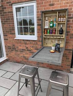 two metal stools sitting next to a table with bottles on it and an open storage unit in the back