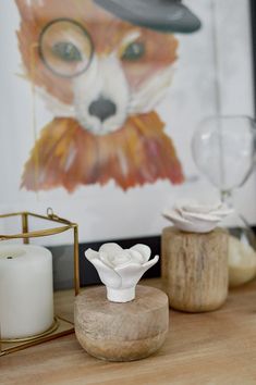 a wooden table topped with vases filled with white flowers and small glass containers next to a painting