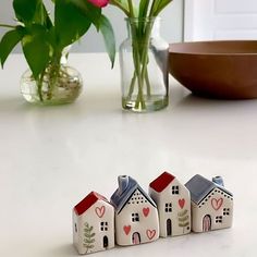 three small houses sitting next to each other on a table with flowers in the background