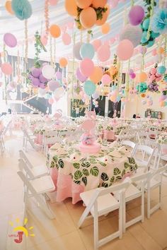 a room filled with lots of tables covered in white and pink tablecloths, balloons hanging from the ceiling