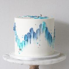 a white cake with blue icing on top of a wooden stand next to a wall