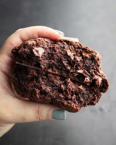 a hand holding a piece of chocolate cake in it's left hand on a gray surface