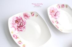 two white plates with pink flowers on them sitting next to each other in front of a white background