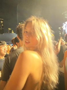 a woman standing in front of a group of people at a music festival with her back to the camera