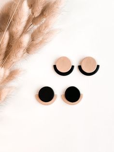 three pairs of black and beige earrings on top of a white surface next to feathers