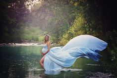 a pregnant woman in a flowing blue dress is standing on the edge of a body of water