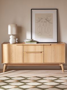 a sideboard with an art print on the wall above it and a lamp next to it