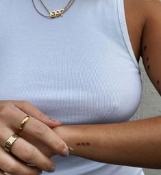 a woman with tattoos on her arm wearing a white tank top and gold bracelets