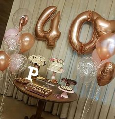 a table topped with lots of balloons and cake next to a number 40 sign on top of a wooden table