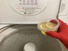 a person in red gloves is holding a plastic cup with lemons on it next to a washing machine