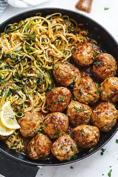 meatballs and noodles in a skillet with lemon wedges on the side, ready to be eaten